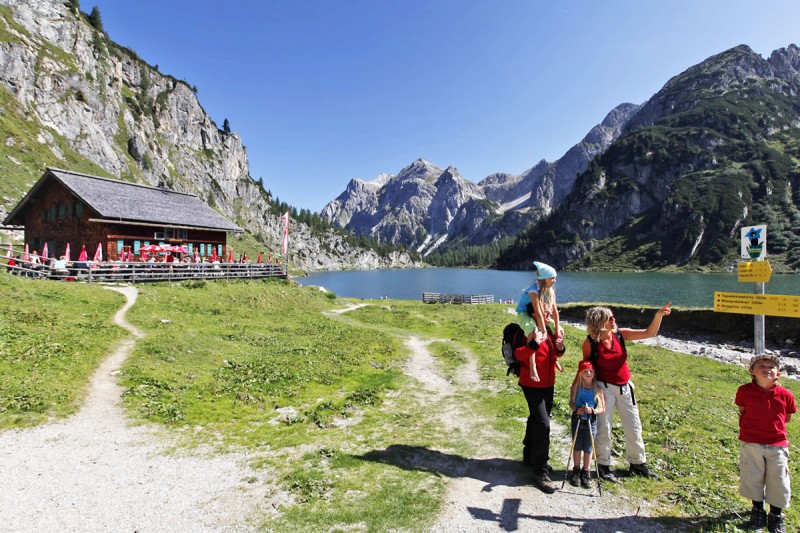 A family hiking in Wagrain, in the background is a mountain hut and lake